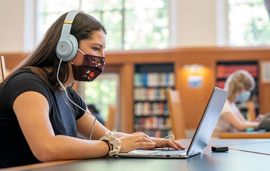 Young female student in mask at a library on computer