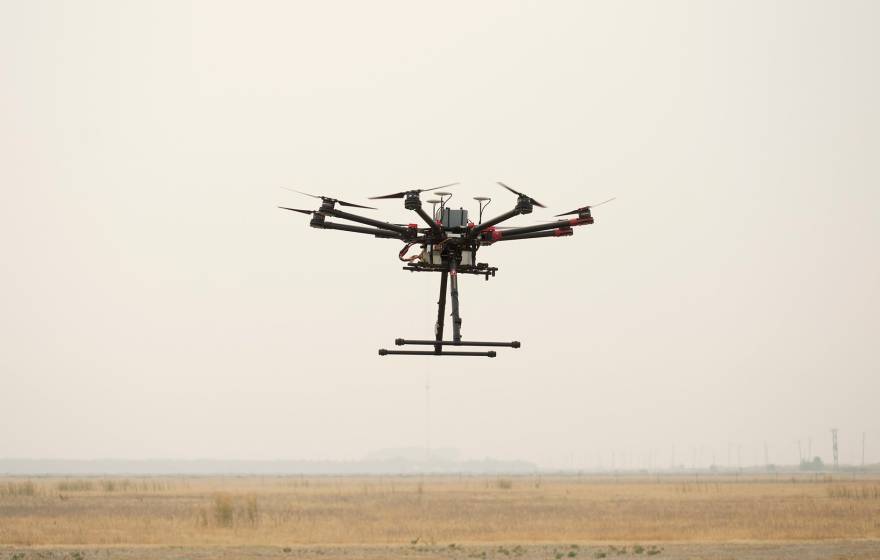 A drone hovers in smoky air over a field