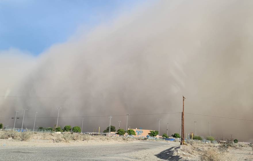 A dust cloud, taking up most of the picture, over a dirt road