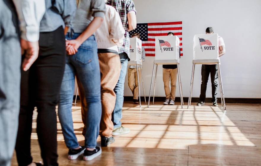 A line of people ready to vote and one person in a booth