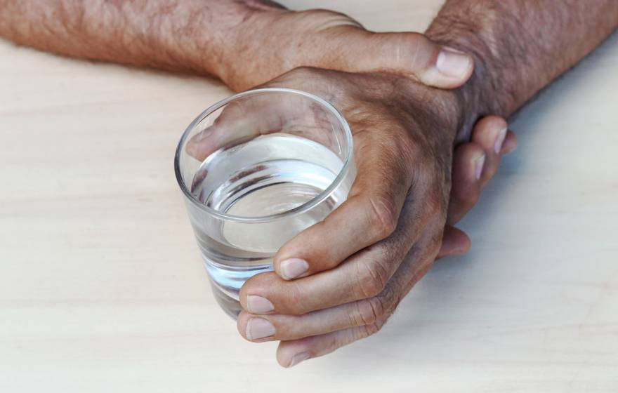 A man steadying a hand holding a glass of water with his other hand