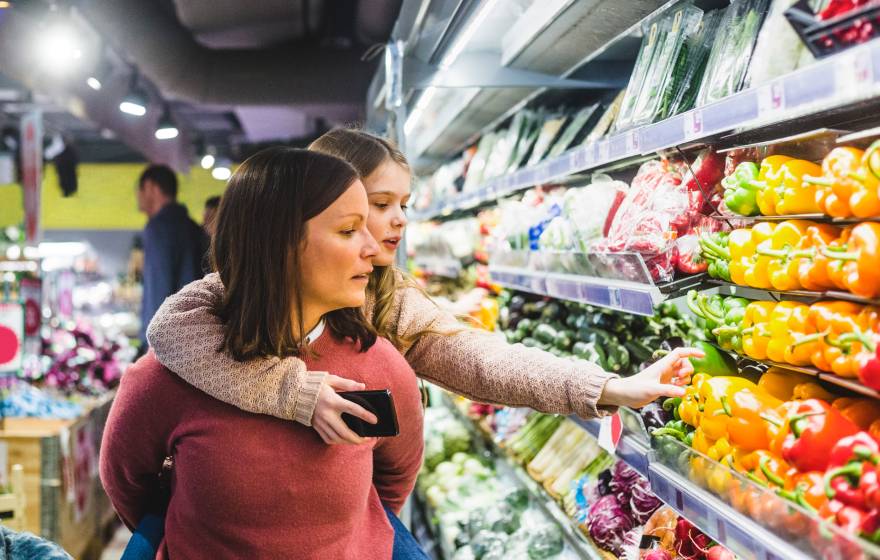 Grocery shopping A child hanging on to her mom's back reaches for a pepper in the produce aisle