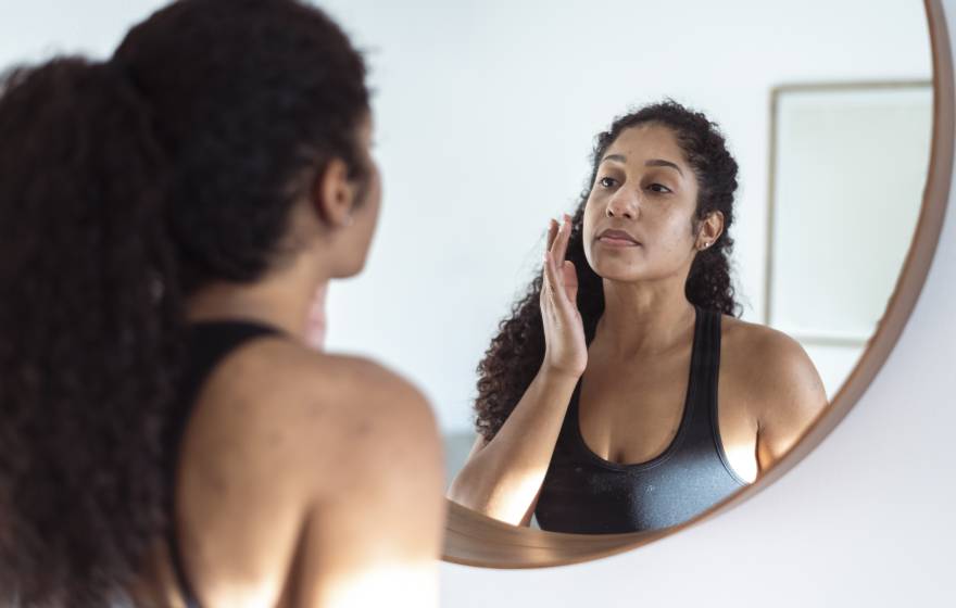Young woman with slight case of acne looks in mirror, touches face, while wearing active wear