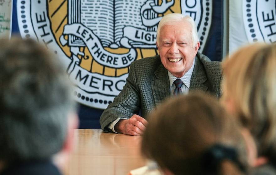 Former President Jimmy Carter, center, smiles broadly as he speaks to an audience around a conference table with the UC Merced official seal behind him