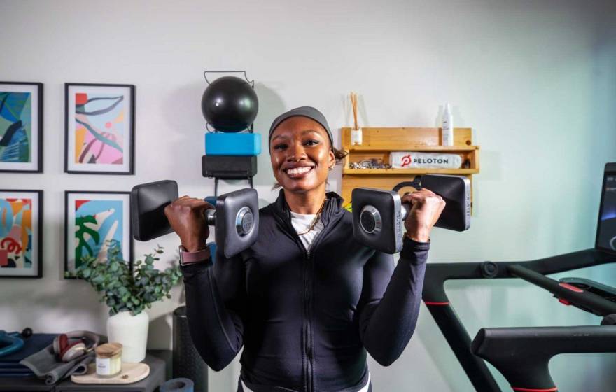 Lauren Patrick smiles at the camera wearing workout attire, holding a dumbbell up in each arm