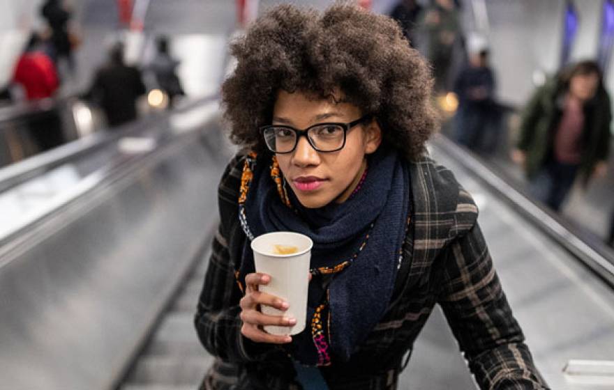 Young woman holding a coffee going up the escalator