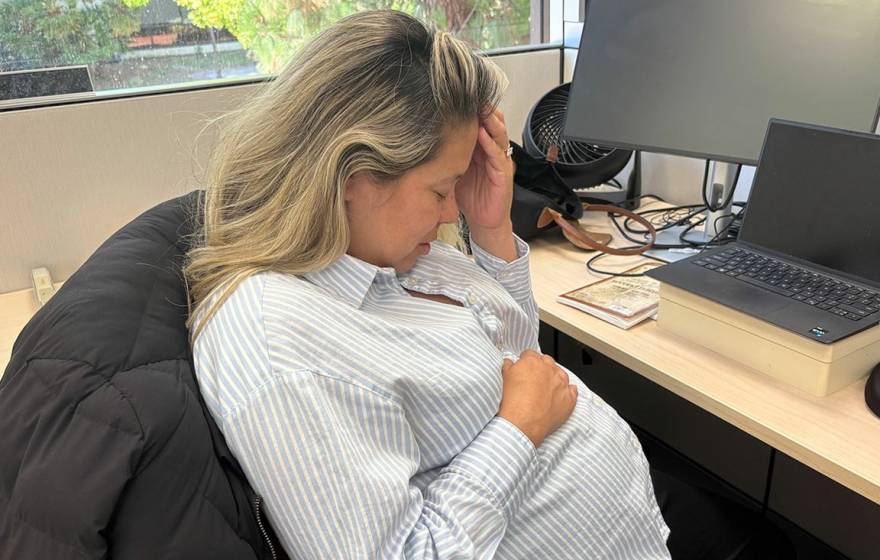 Morning sickness A woman holds her head with another hand over her pregnant belly while sitting at a desk in an office
