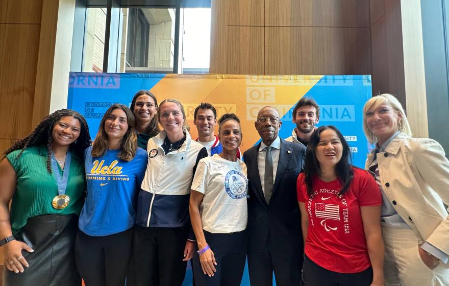 Olympian and Paralympian athletes stand with President Drake and Board of Regents Chair Janet Reilly in front of a University of California backdrop for photos