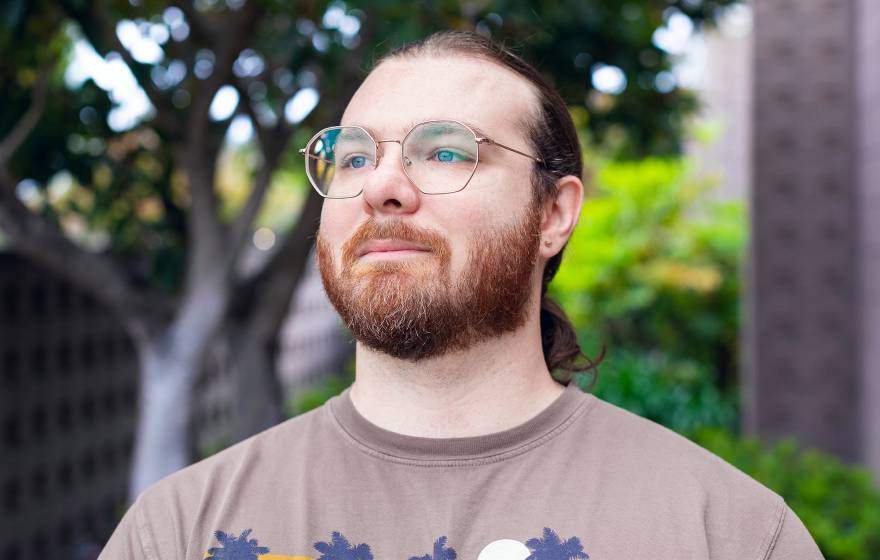 A man with a beard and pony tail wearing a T-shirt and glasses gazing into the distance