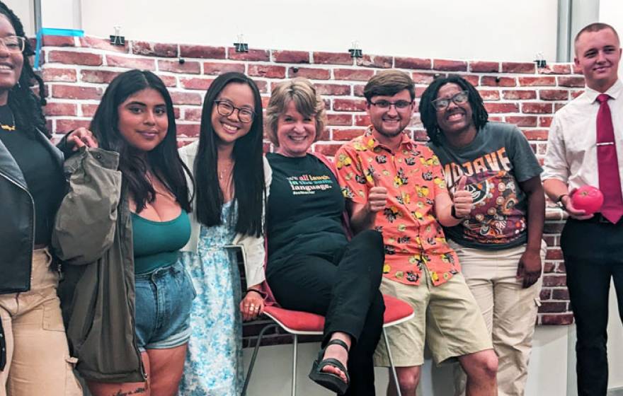 Six students and a professor on a standup comedy set, smiling for the camera with arms around each other