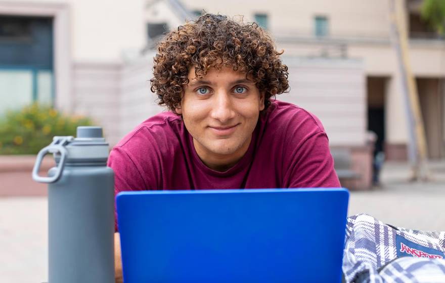 Learning curiosity A young man with curly hair stares intently above a laptop while sitting outdoors