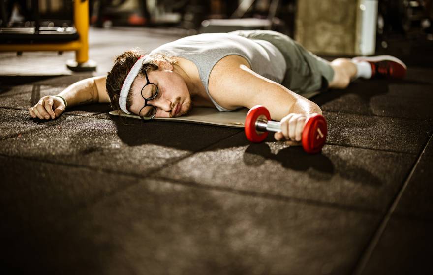 Male athlete lying on the floor, feeling exhausted after sports training with dumbbells in a gym