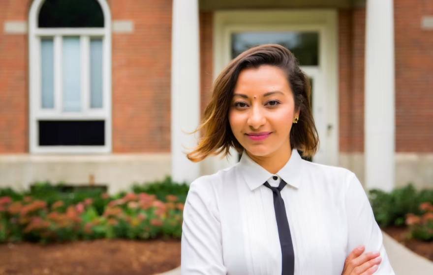 Study on Mexican American families A woman with a skinny tie and arms crossed smiles at camera