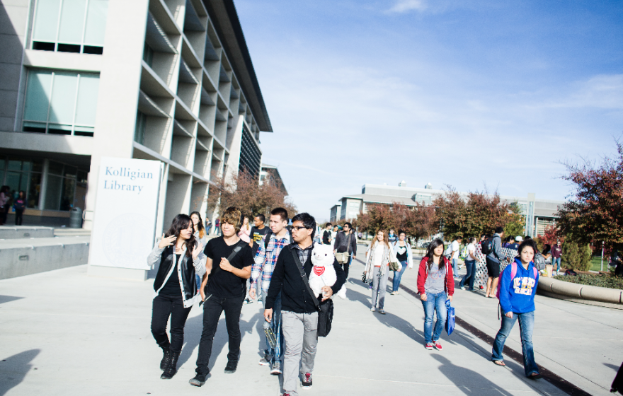 A group of students walking along the UC Merced campus, blue sky in background