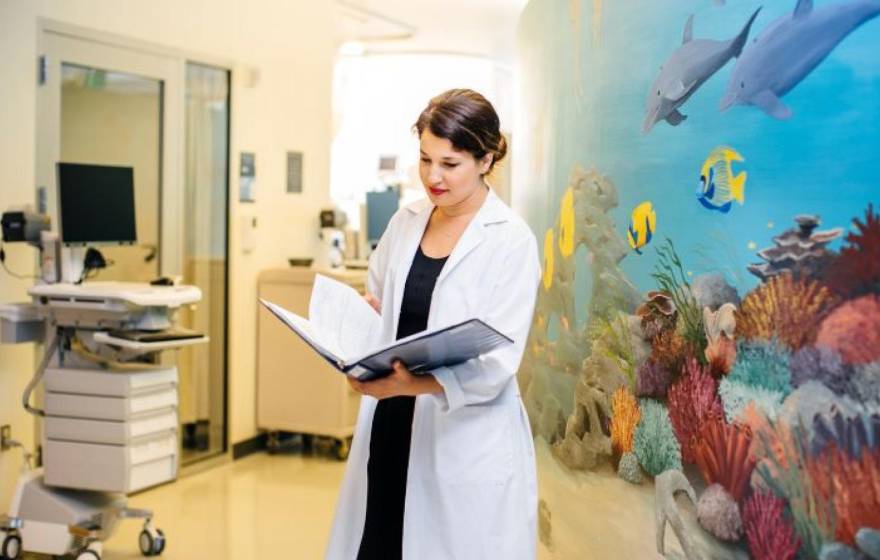 Woman doctor in white coat looks at a medical record with a colorful wall with an undersea mural behind her