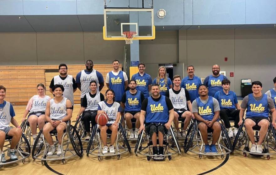 Group photo of the UCLA wheelchair basketball group in front of a basketball net