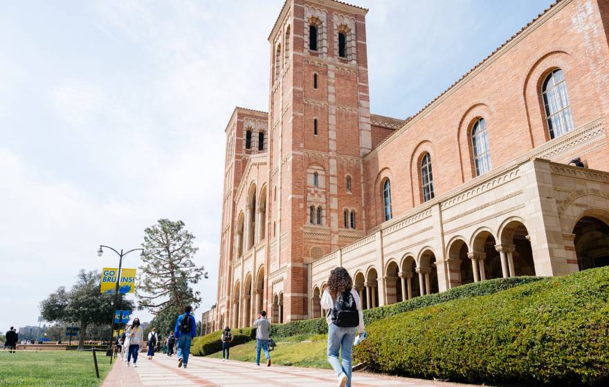 Royce Hall on the UCLA campus, a light adobe brick building, photographed from a low angle and at the side as a few students walk