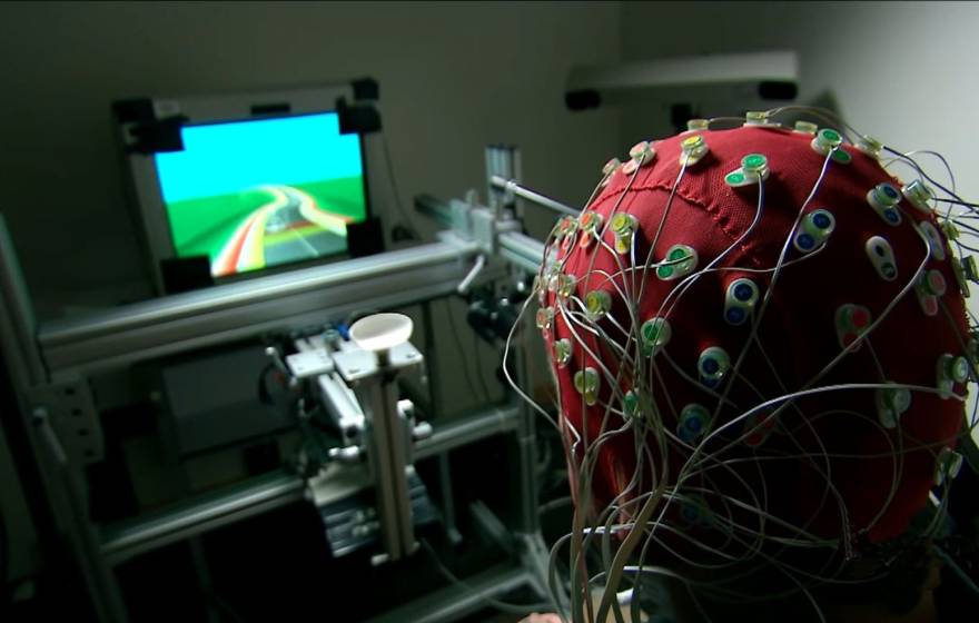 Someone with a cap for monitoring brain activity on their head plays a video game
