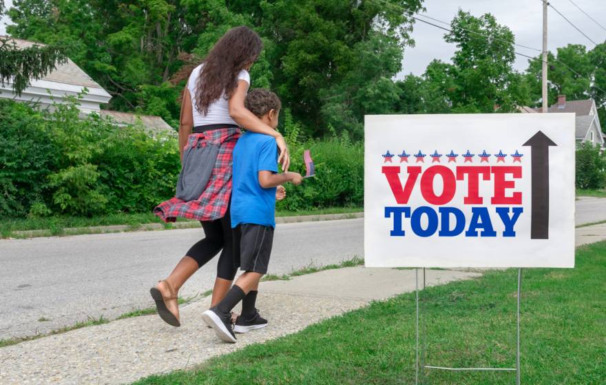 A Black woman and her son walk past a Vote Today sign to the polls