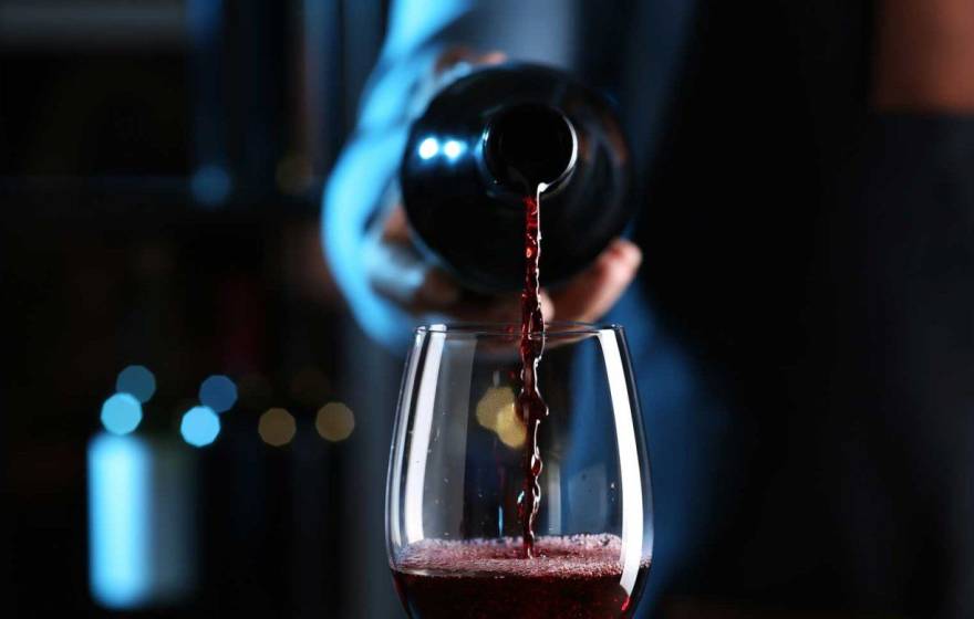 Is there a healthy amount to drink A hand pours a bottle of red wine into a wine glass, centered