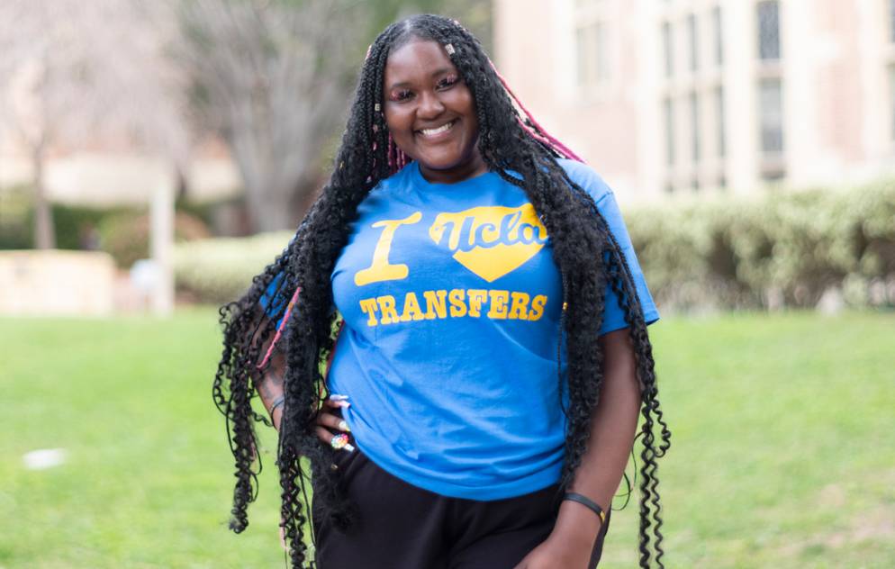 A student wearing an "I heart UCLA transfers" t-shirt stands in front of a building on the UCLA campus