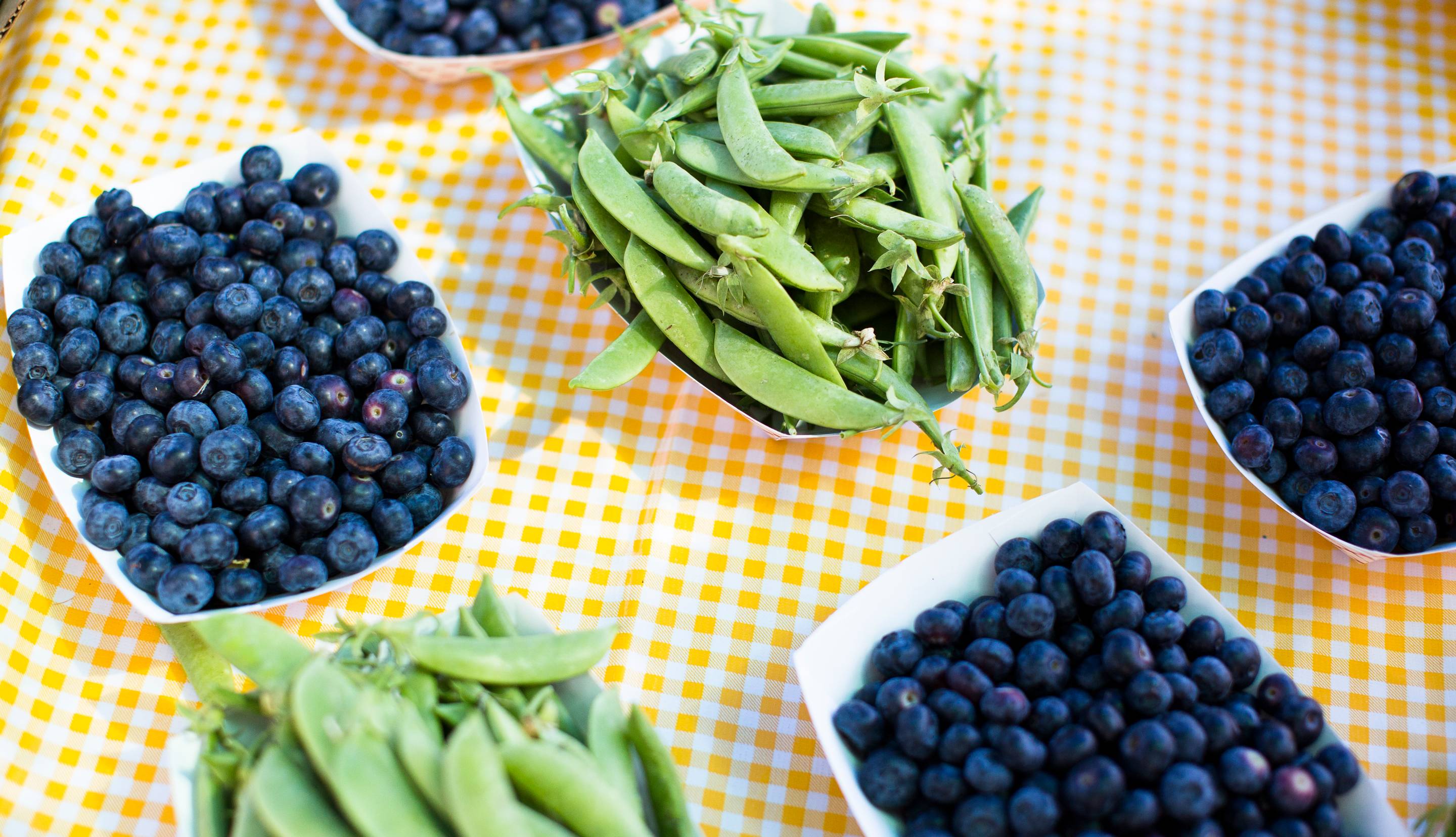 Blueberries and green beans in paper trays on a yellow checked tablecloth