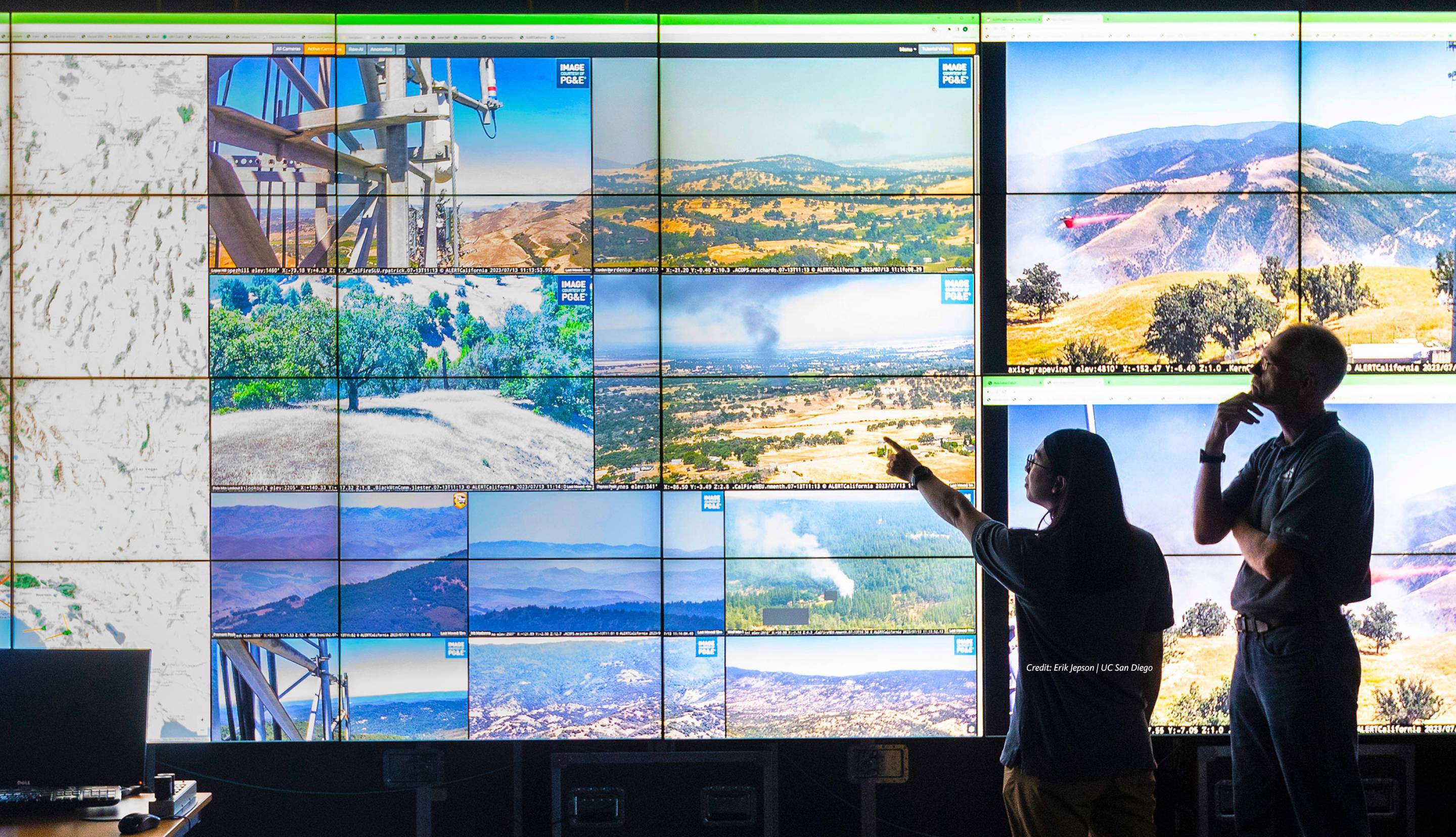 Two people stand in front of a wall of screens showing footage of California landscapes
