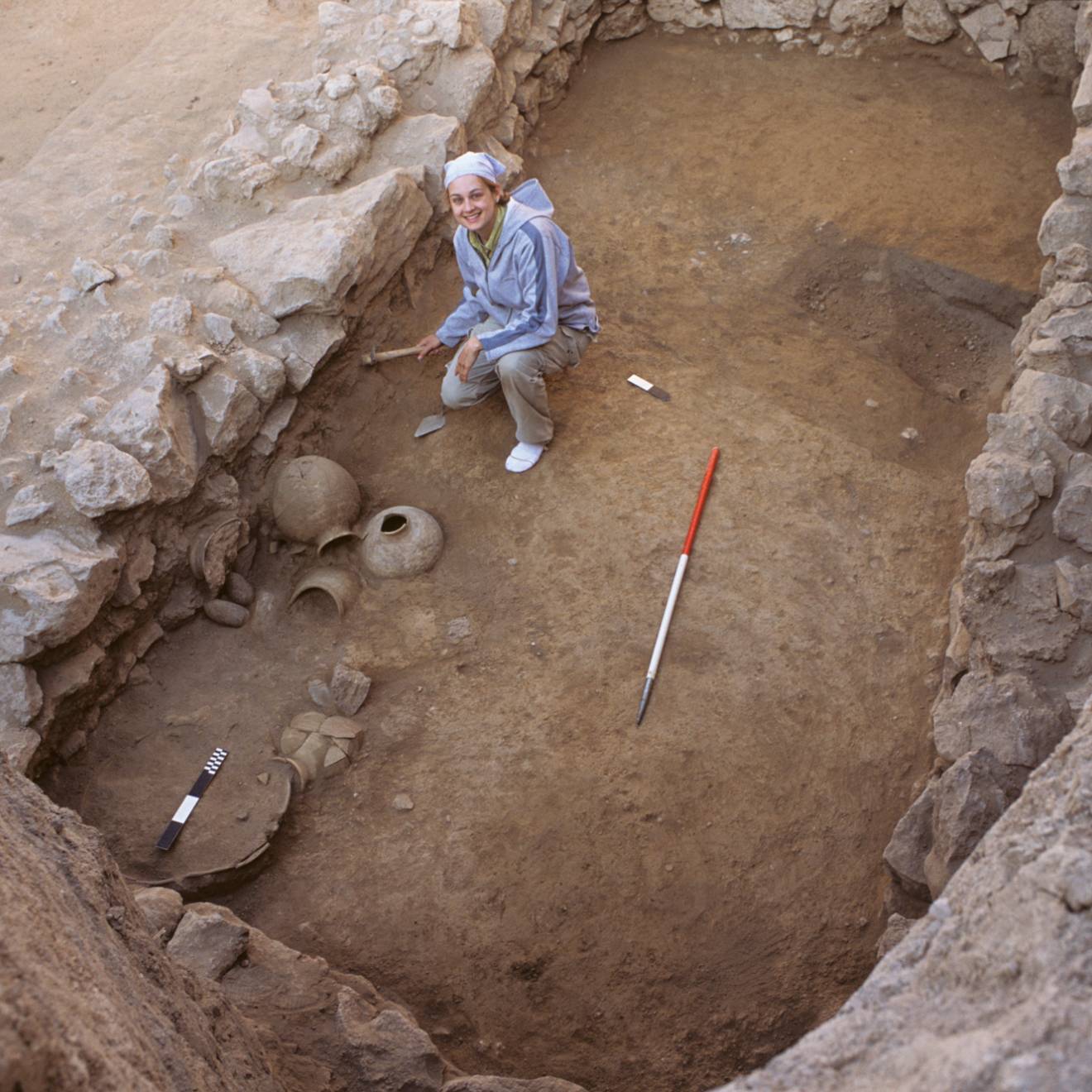 A woman in a very ancient, shallow tomb, looks up from her excavating work, smiling