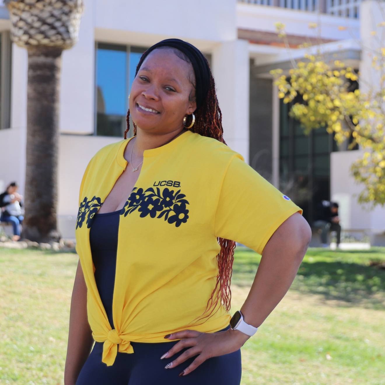 A smiling woman in a yellow UCSB shirt standing in front of a building on campus