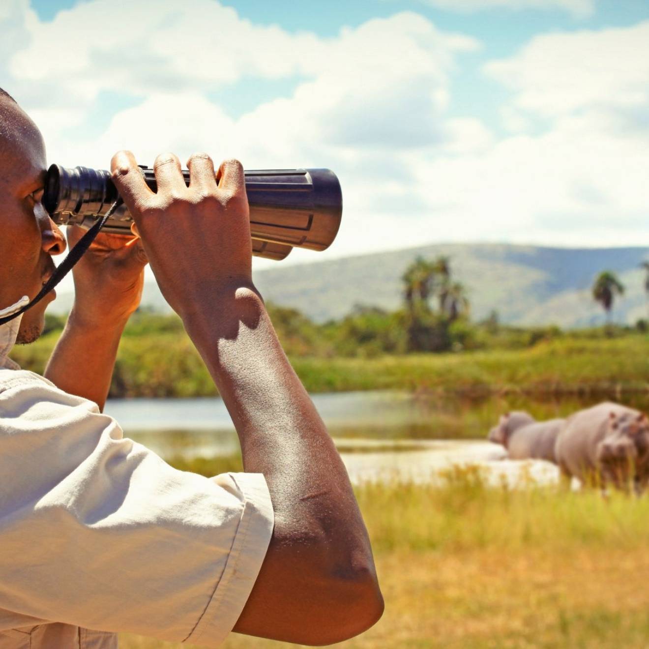 A man in profile looks through binoculars while standing in a field