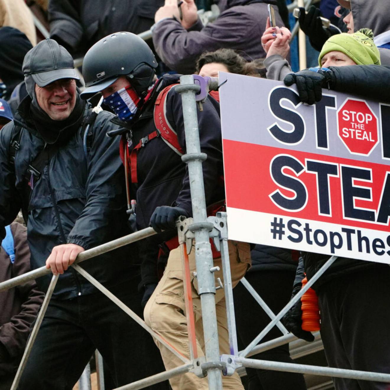 People wearing tactical gear attack the Capitol on Jan 6th, with a big sign reading "Stop the Steal"