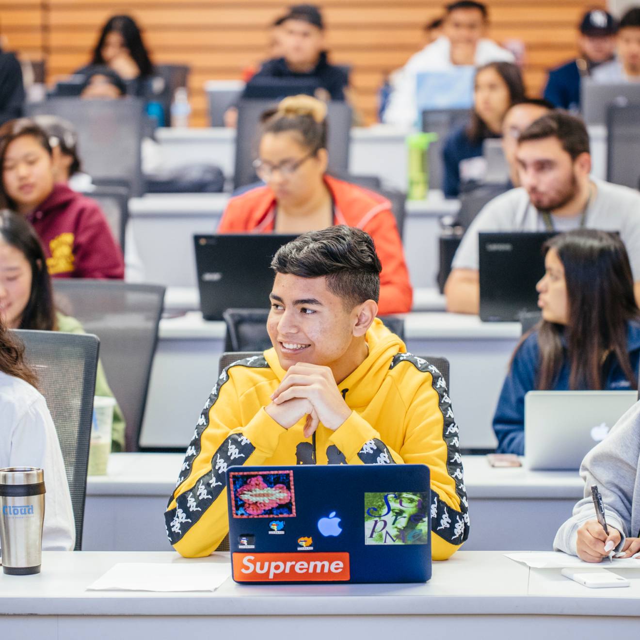 students sitting in a lecture hall listening and engaged, each with an open laptop