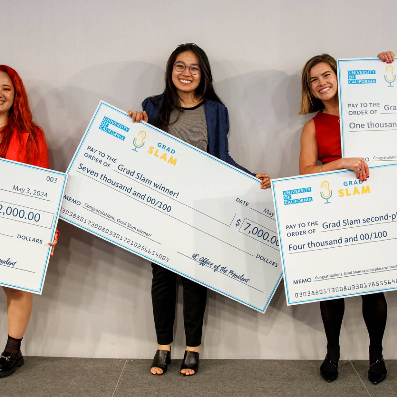 Three people standing holding giant checks