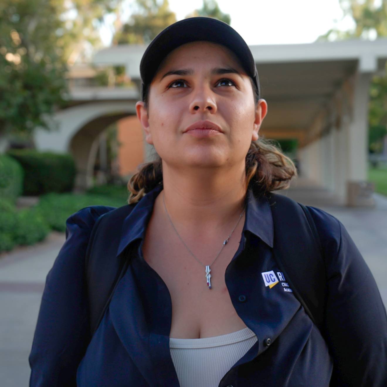 A woman wearing a baseball cap and walking on the UC Riverside campus looks up