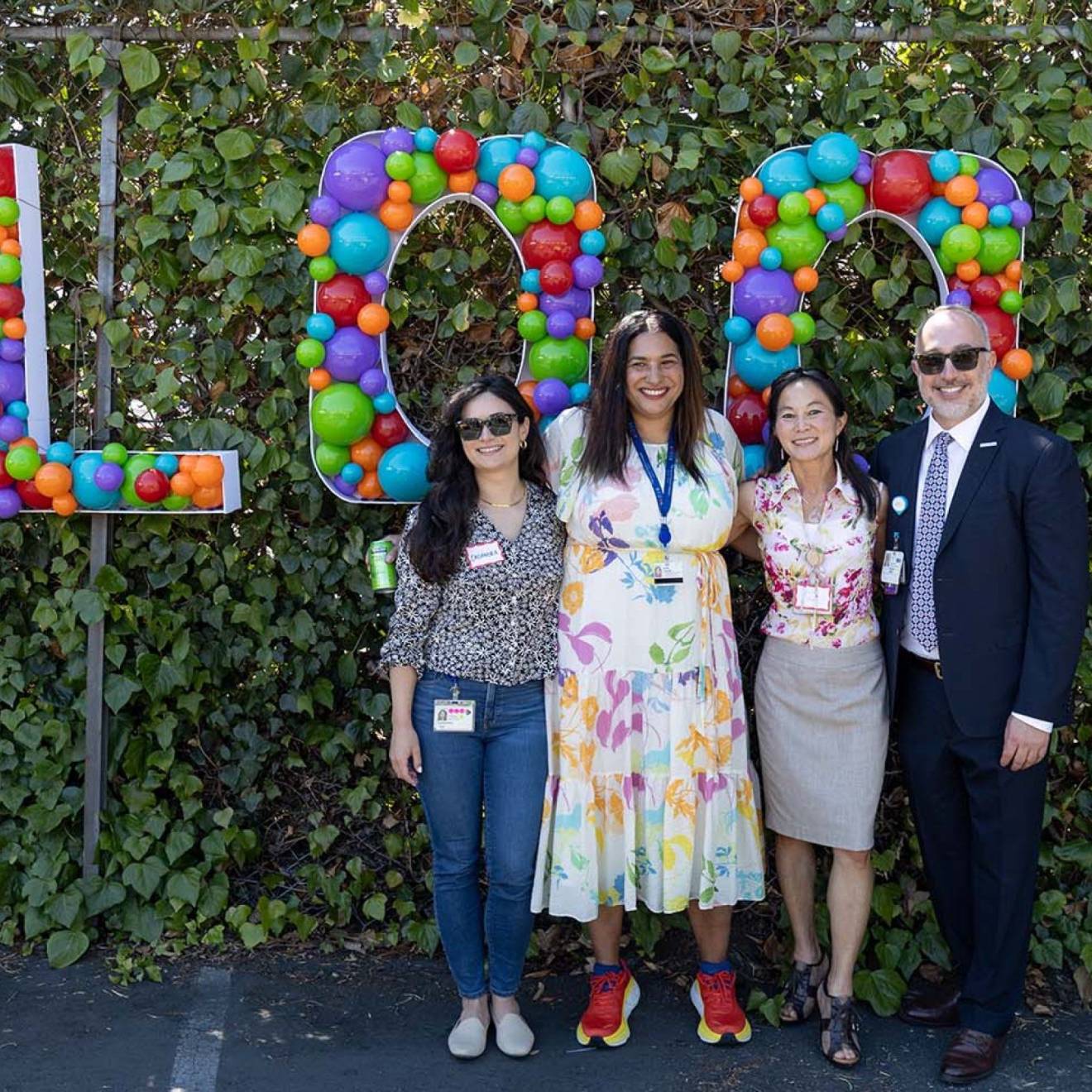 Four people outdoors in front of a sign made of balloons that says 'Bloom'