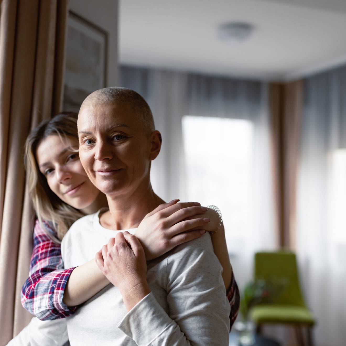 A grown child holds her mother, who has little hair on her head