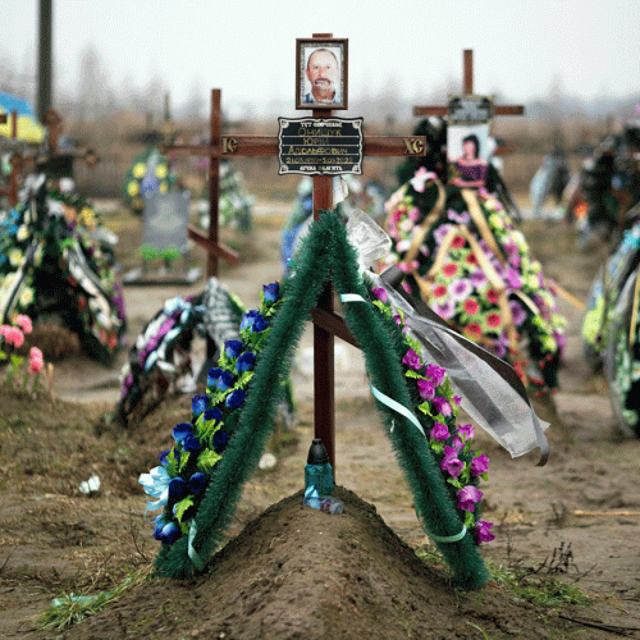 Photos on crosses covered in flowers mark graves in Bucha, Ukraine