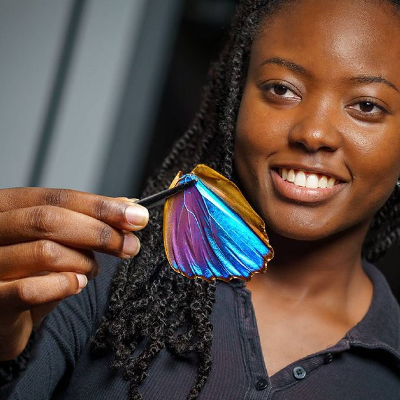 Young woman with braids smiling holds up a Morpho butterfly