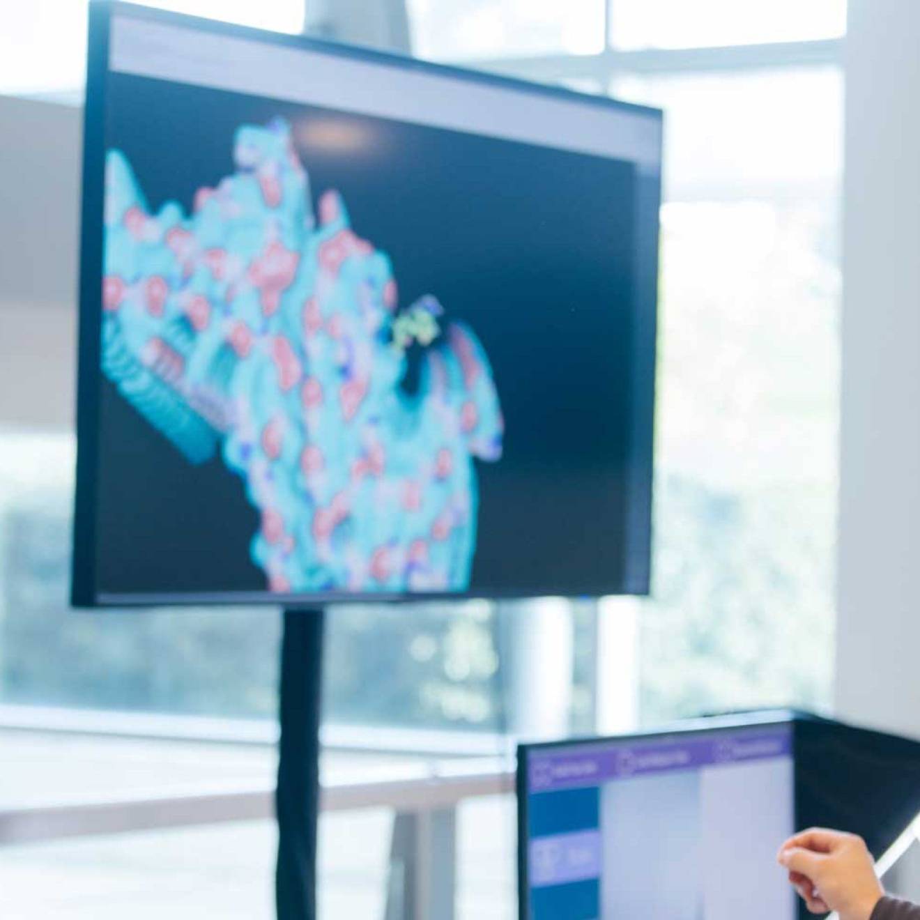 CRISPR approach Someone wearing a virtual reality headset in front of two large screens showing molecules and one smaller screen