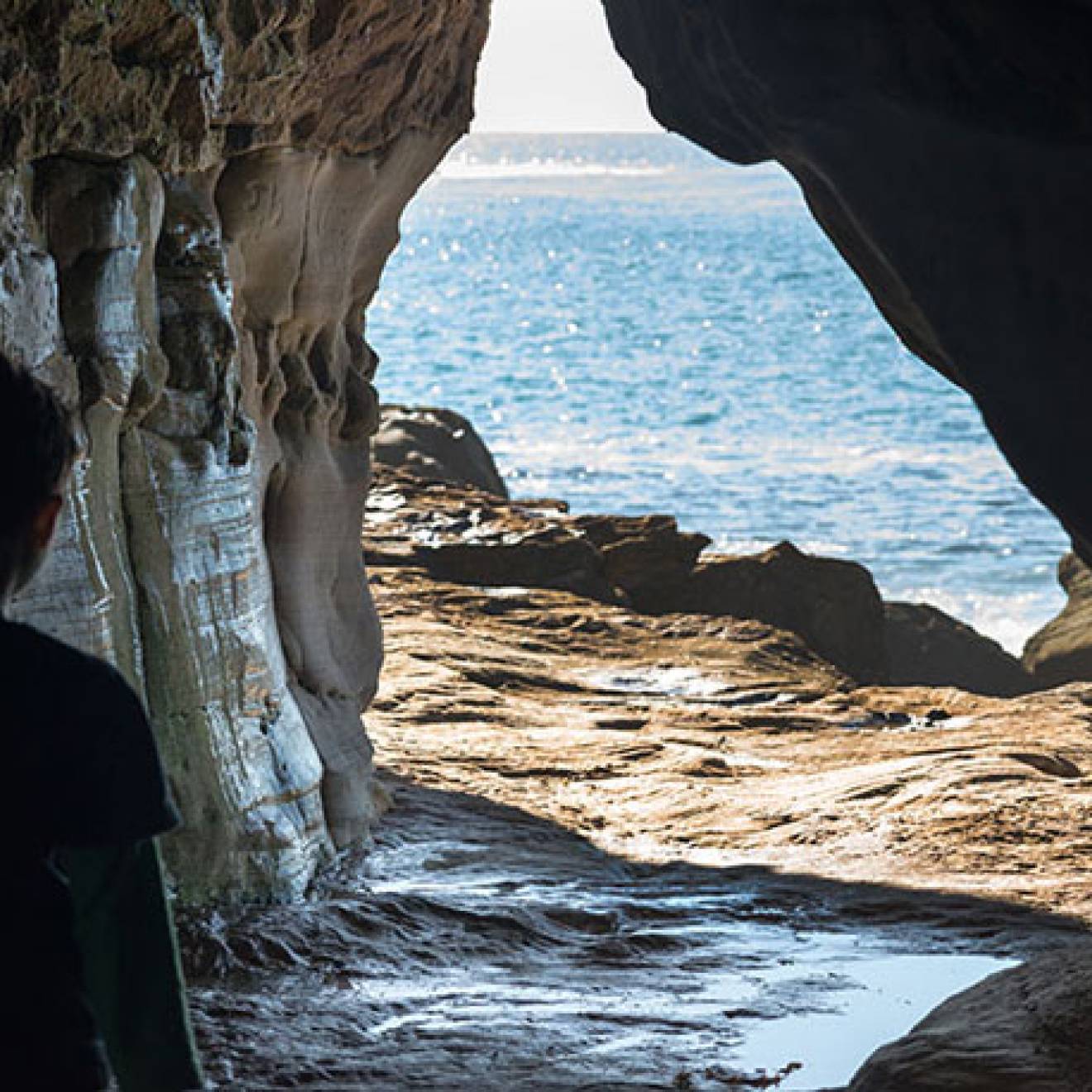 Person looking out from a cave at water