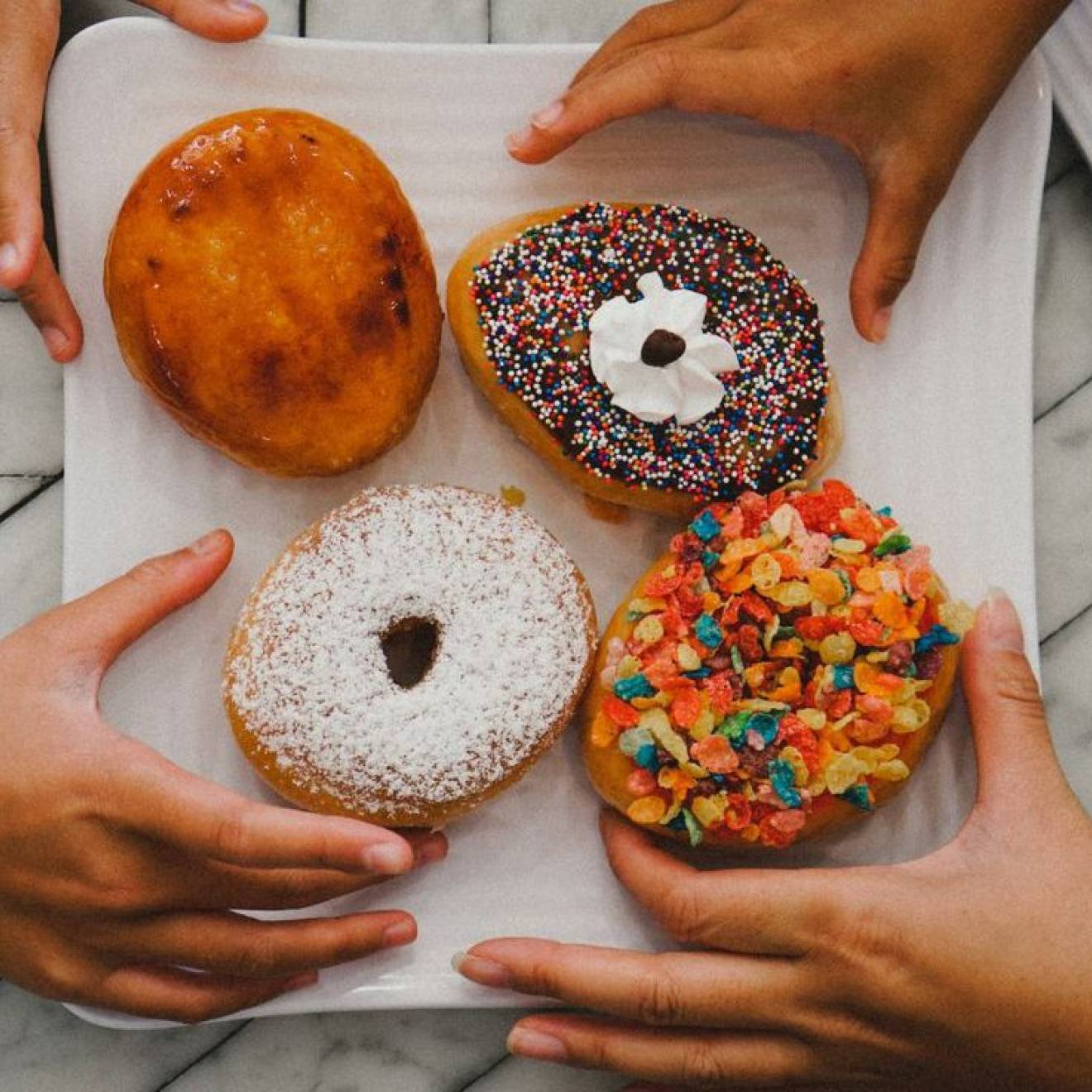 Multiple hands reaching for donuts