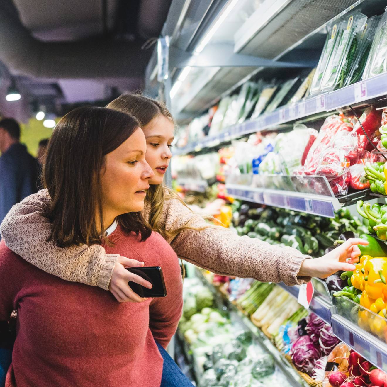 Grocery shopping A child hanging on to her mom's back reaches for a pepper in the produce aisle
