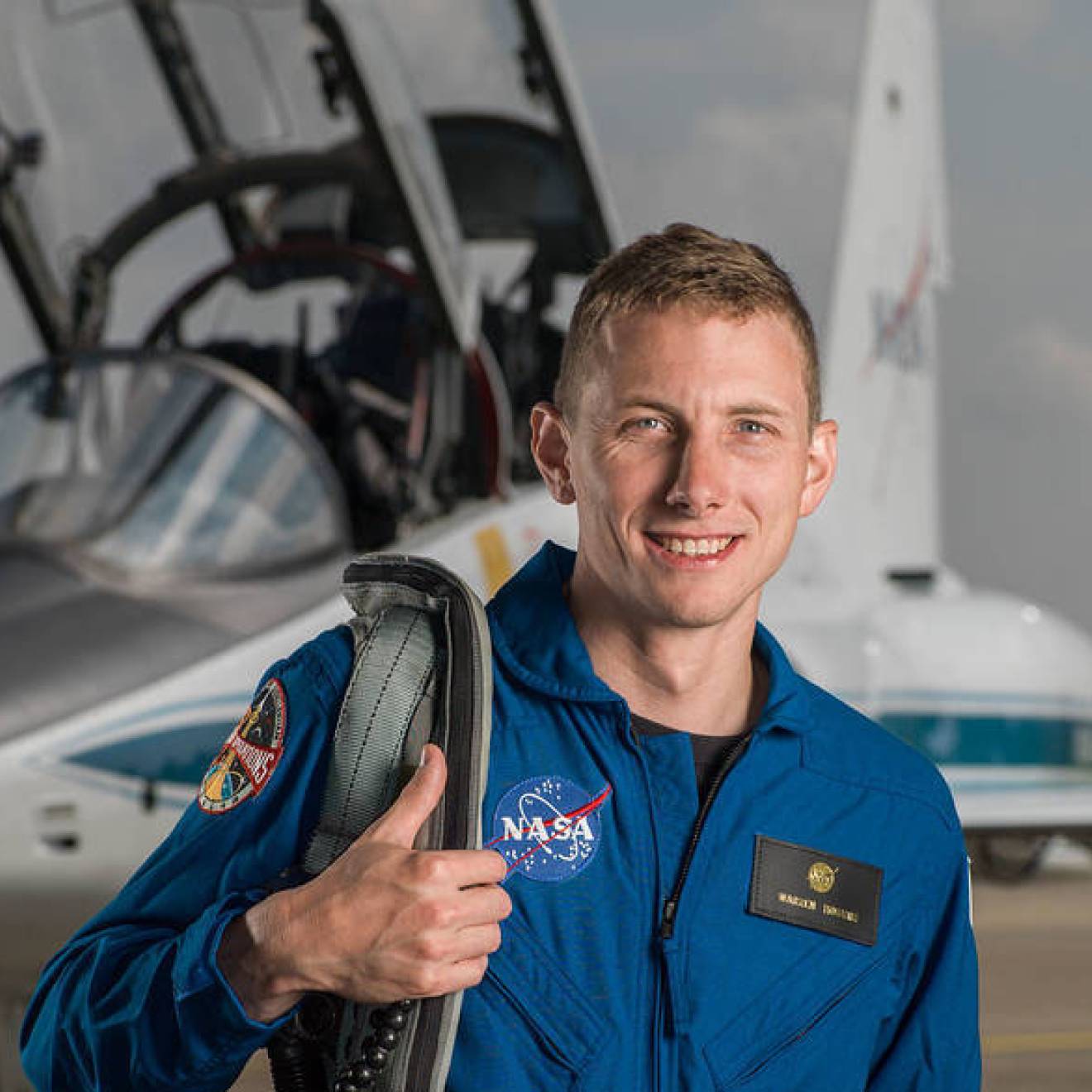 Warren Hoburg in blue spacesuit in front of an aircraft