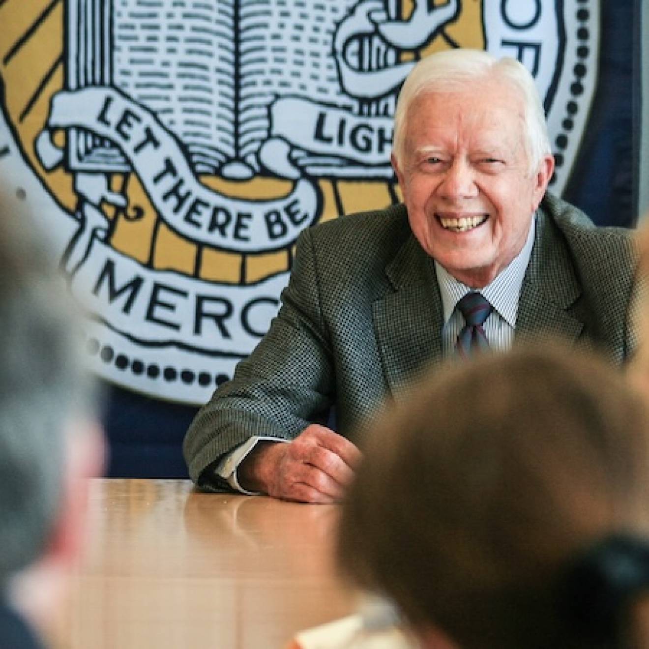 Former President Jimmy Carter, center, smiles broadly as he speaks to an audience around a conference table with the UC Merced official seal behind him