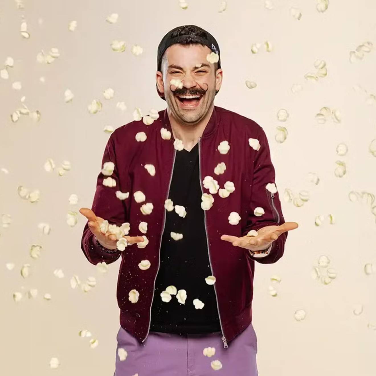 Joe Sasto Laughing man in magneta jacket and mustache while pasta chips fall around him