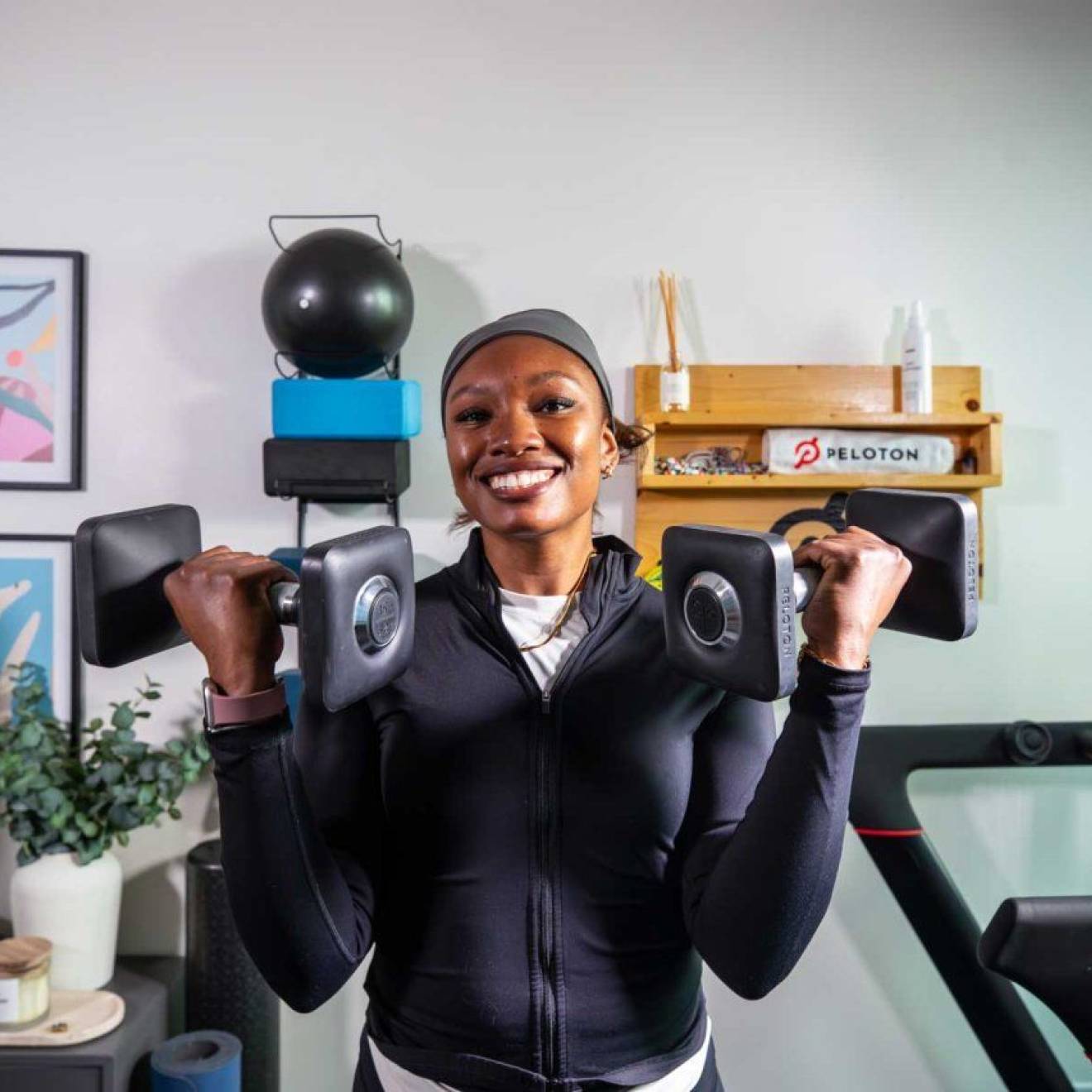 Lauren Patrick smiles at the camera wearing workout attire, holding a dumbbell up in each arm