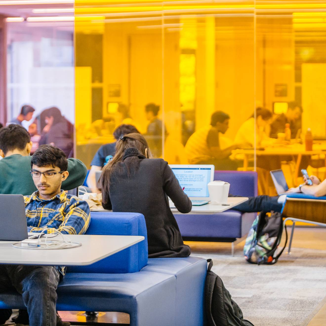 students working on laptop computers at tables in a large study space