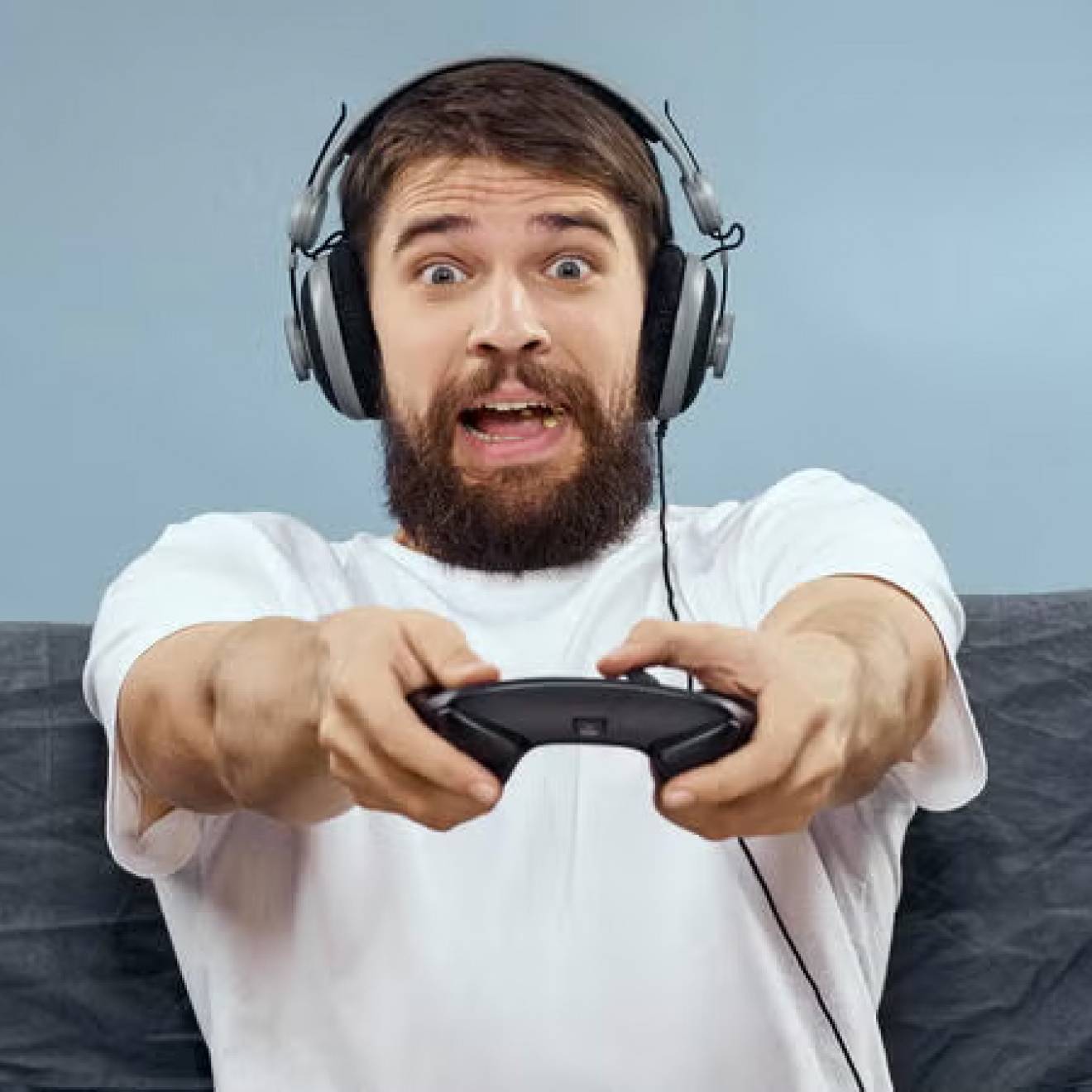 A man sitting on a couch with headphones on holding a video game controller with a surprised, frightened expression