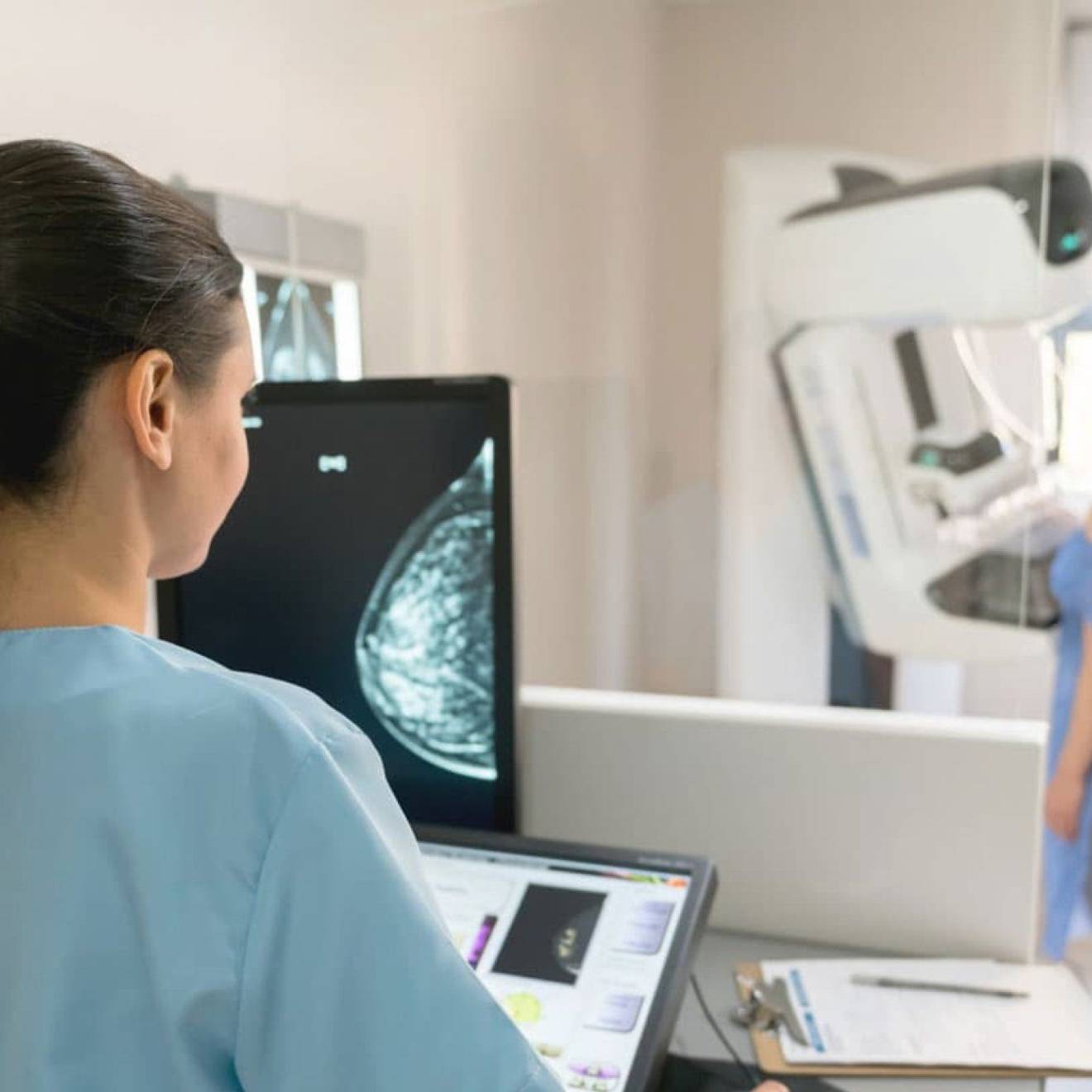 Nurse and patient conducting a mammogram, patient in front of machine