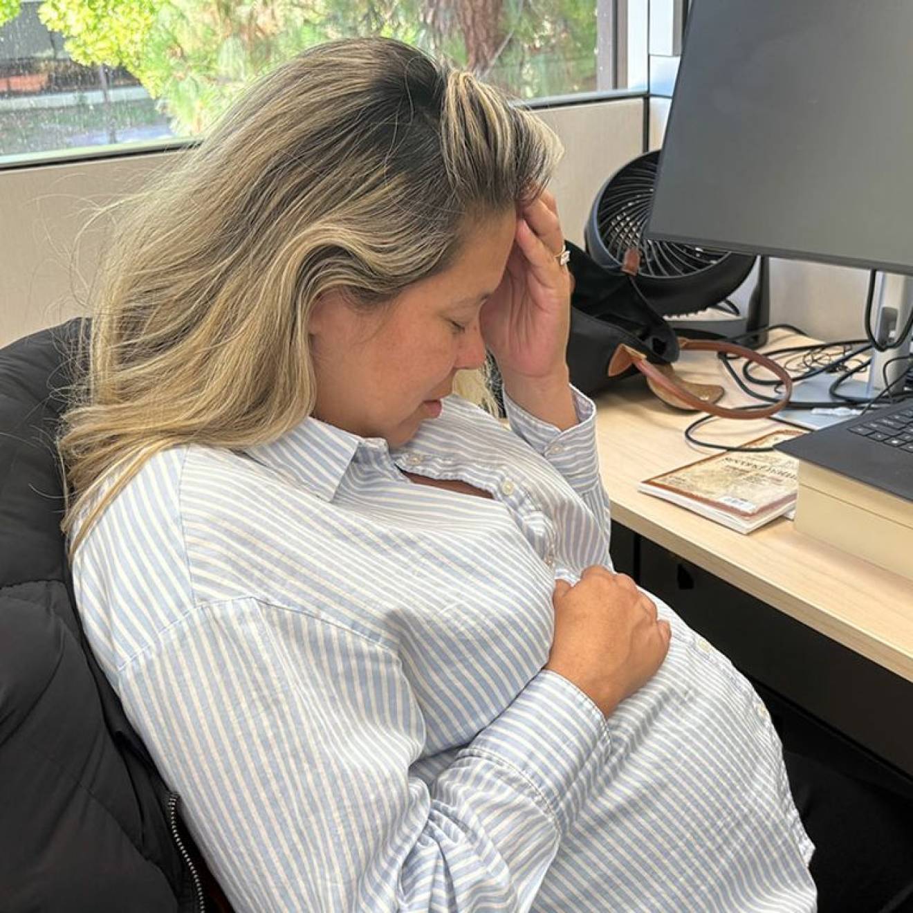 Morning sickness A woman holds her head with another hand over her pregnant belly while sitting at a desk in an office